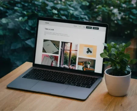 Macbook Pro laptop on timber desk with screen open. Green plants in the background